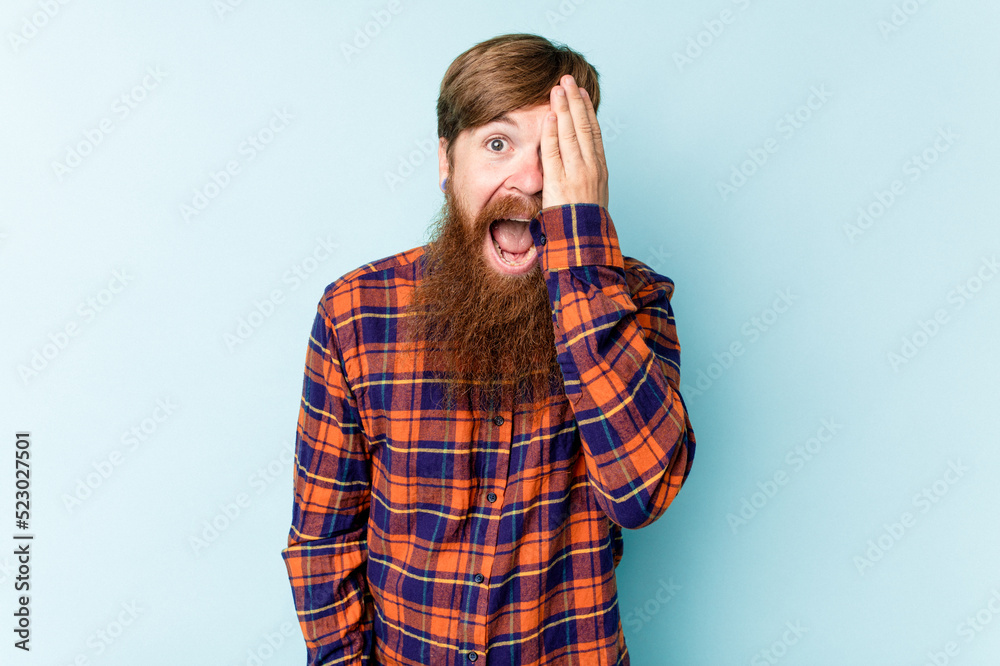 Young caucasian red-haired man isolated on blue background having fun covering half of face with palm. Young caucasian red-haired man isolated on blue background having fun covering half of face with palm.