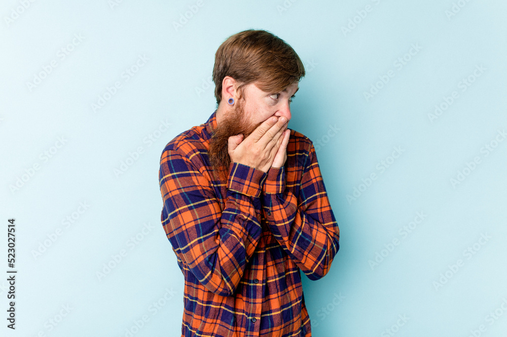 Young caucasian red-haired man isolated on blue background laughing about something, covering mouth with hands. Young caucasian red-haired man isolated on blue background laughing about something, covering mouth with hands.