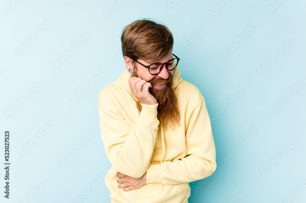 Young caucasian red-haired man isolated on blue background laughs happily and has fun keeping hands on stomach. Young caucasian red-haired man isolated on blue background laughs happily and has fun keeping hands on stomach.