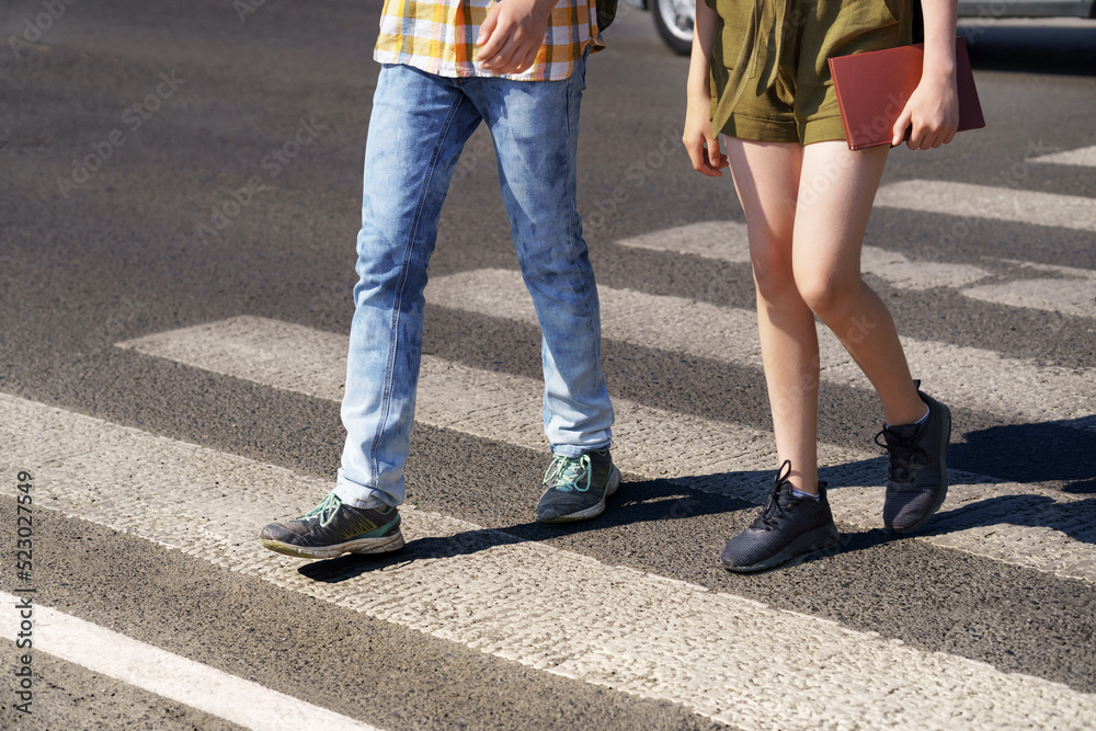 teenage schoolchildren, a boy and a girl cross the road at a pedestrian crossing