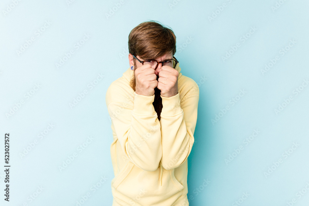 Young caucasian red-haired man isolated on blue background throwing a punch, anger, fighting due to an argument, boxing. Young caucasian red-haired man isolated on blue background throwing a punch, anger, fighting due to an argument, boxing.