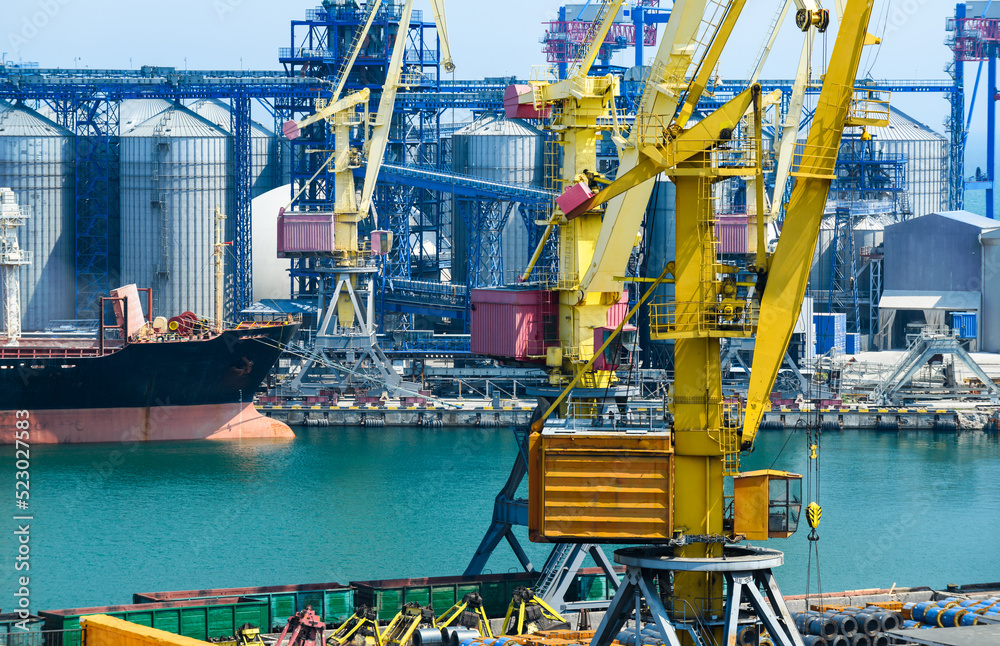 Fototapeta premium industrial infrastructure of the seaport, the sea, cranes and railway wagons, grain silo, bulk carrier vessel and grain storage elevators, the concept of sea cargo transportation