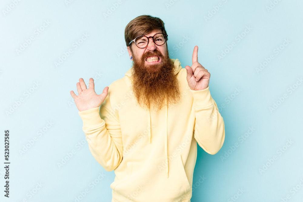 Young caucasian red-haired man isolated on blue background holding and showing a product on hand. Young caucasian red-haired man isolated on blue background holding and showing a product on hand.