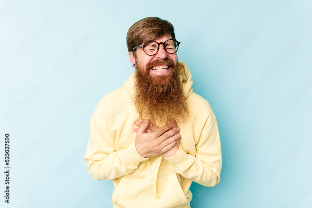 Young caucasian red-haired man isolated on blue background laughs out loudly keeping hand on chest. Young caucasian red-haired man isolated on blue background laughs out loudly keeping hand on chest.