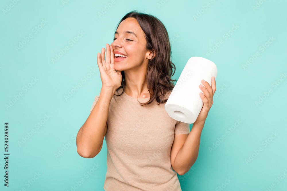 Young hispanic woman holding kitchen roll isolated on blue background shouting and holding palm near opened mouth.