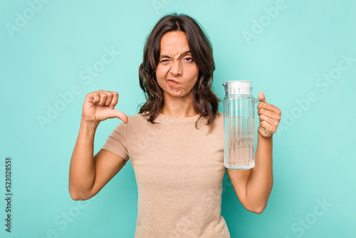 Young hispanic woman holding a water of jar isolated on blue background showing a dislike gesture, thumbs down. Disagreement concept.