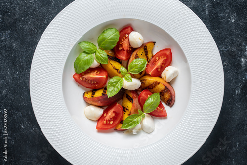 Grilled peach salad with mozzarella, tomato, green basil and sauce, close up, top view
