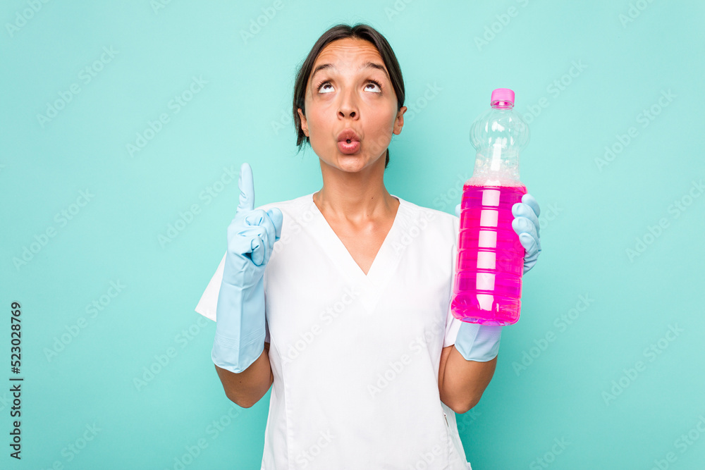Young cleaner hispanic woman isolated on blue background pointing upside with opened mouth. Young cleaner hispanic woman isolated on blue background pointing upside with opened mouth.