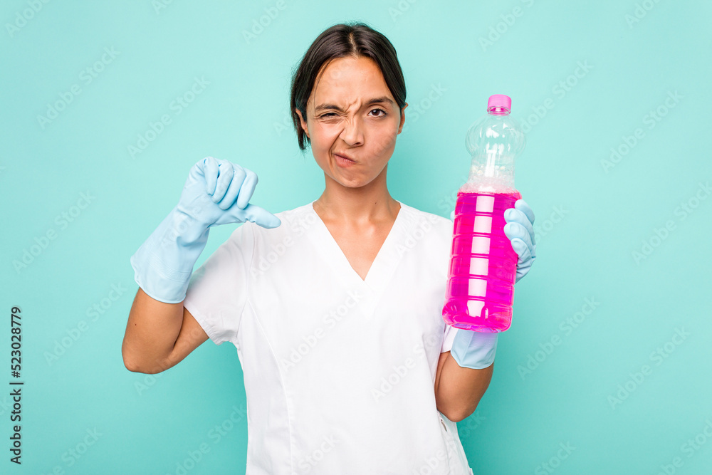 Young cleaner hispanic woman isolated on blue background showing a dislike gesture, thumbs down. Disagreement concept. Young cleaner hispanic woman isolated on blue background showing a dislike gesture, thumbs down. Disagreement concept.