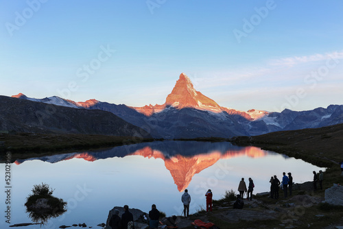 Sihlouettes of campers and photographers at the Stellisee lake watching the alpenglow of the sunrise on the Matterhorn.
