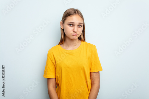Young caucasian girl isolated on blue background blows cheeks, has tired expression. Facial expression concept.