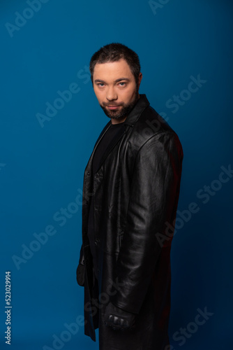 portrait of a man in a black leather coat. model with a beard on a blue background. black hair