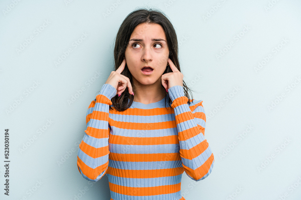 Young caucasian woman isolated on blue background covering ears with fingers, stressed and desperate by a loudly ambient. Young caucasian woman isolated on blue background covering ears with fingers, stressed and desperate by a loudly ambient.