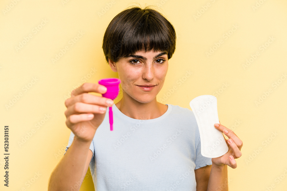 Young caucasian woman holding a menstrual cup isolated on yellow background Young caucasian woman holding a menstrual cup isolated on yellow background