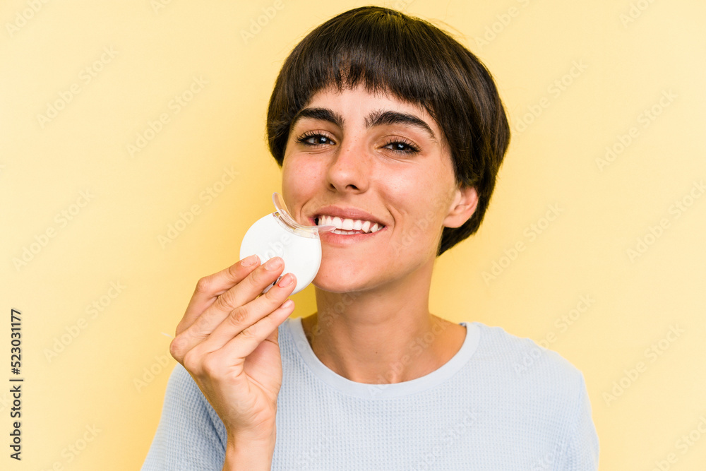 Young caucasian woman holding teeth whitener isolated on yellow background Young caucasian woman holding teeth whitener isolated on yellow background