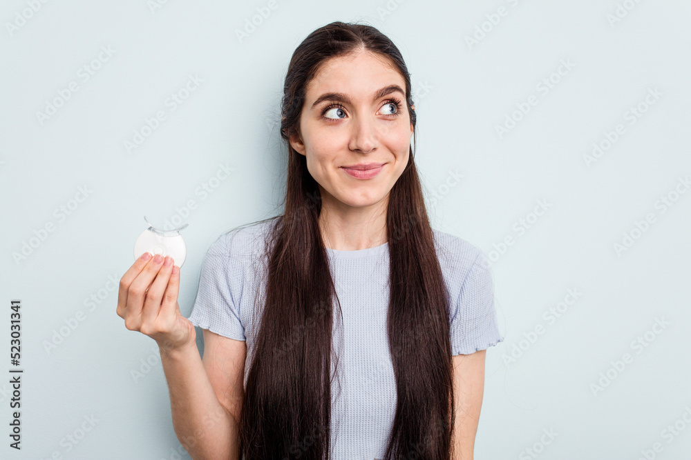 Young caucasian woman holding teeth whitener isolated on blue background dreaming of achieving goals and purposes Young caucasian woman holding teeth whitener isolated on blue background dreaming of achieving goals and purposes