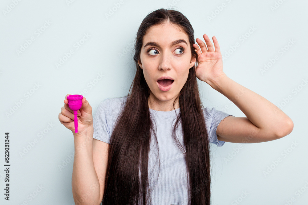 Young caucasian woman holding a sanitary napkin isolated on blue background trying to listening a gossip. Young caucasian woman holding a sanitary napkin isolated on blue background trying to listening a gossip.