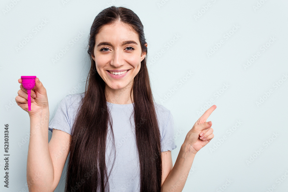 Young caucasian woman holding a sanitary napkin isolated on blue background smiling and pointing aside, showing something at blank space. Young caucasian woman holding a sanitary napkin isolated on blue background smiling and pointing aside, showing something at blank space.