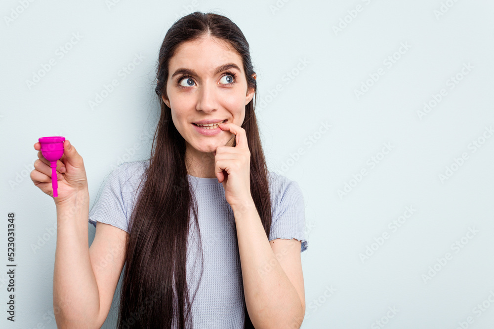 Young caucasian woman holding a sanitary napkin isolated on blue background relaxed thinking about something looking at a copy space. Young caucasian woman holding a sanitary napkin isolated on blue background relaxed thinking about something looking at a copy space.