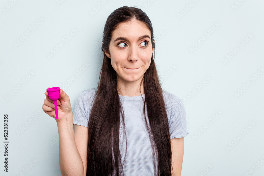 Young caucasian woman holding a sanitary napkin isolated on blue background confused, feels doubtful and unsure. Young caucasian woman holding a sanitary napkin isolated on blue background confused, feels doubtful and unsure.