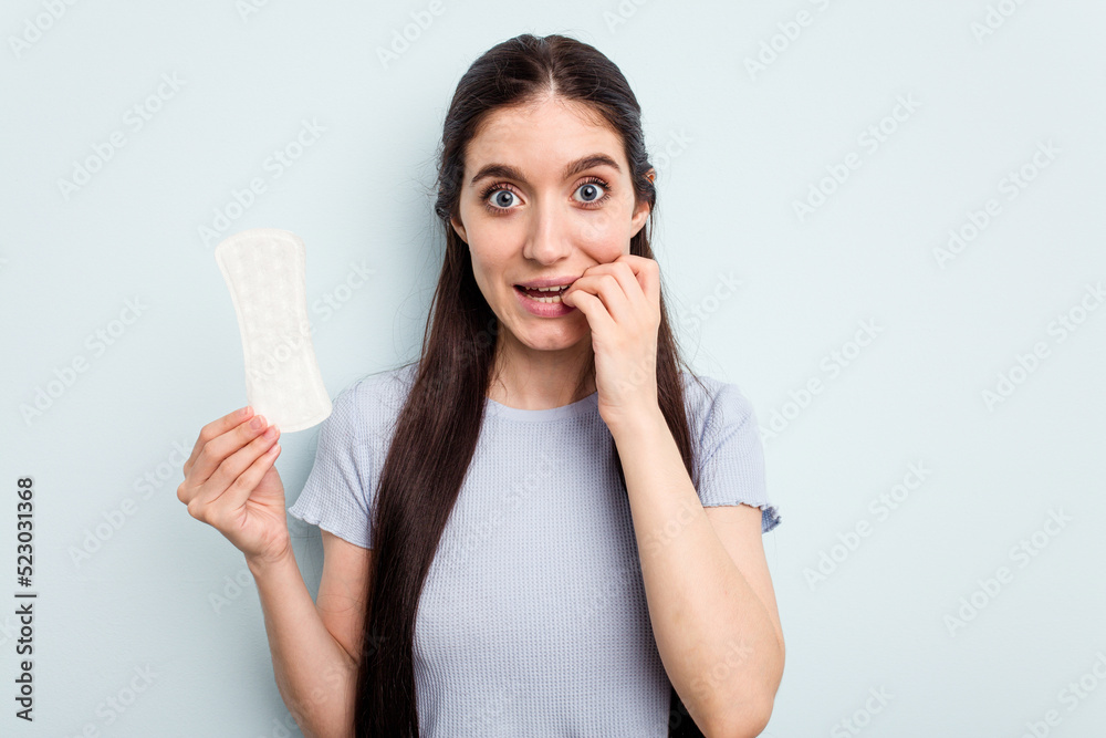 Young caucasian woman holding a sanitary napkin isolated on blue background biting fingernails, nervous and very anxious. Young caucasian woman holding a sanitary napkin isolated on blue background biting fingernails, nervous and very anxious.