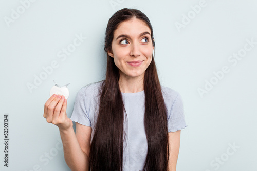 Young caucasian woman holding teeth whitener isolated on blue background dreaming of achieving goals and purposes