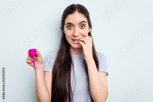 Young caucasian woman holding a sanitary napkin isolated on blue background biting fingernails, nervous and very anxious.