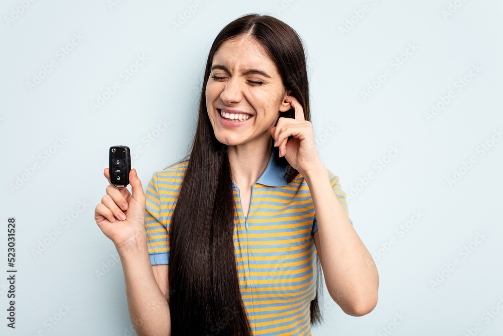 Young caucasian woman holding car keys isolated on blue background covering ears with hands. Young caucasian woman holding car keys isolated on blue background covering ears with hands.