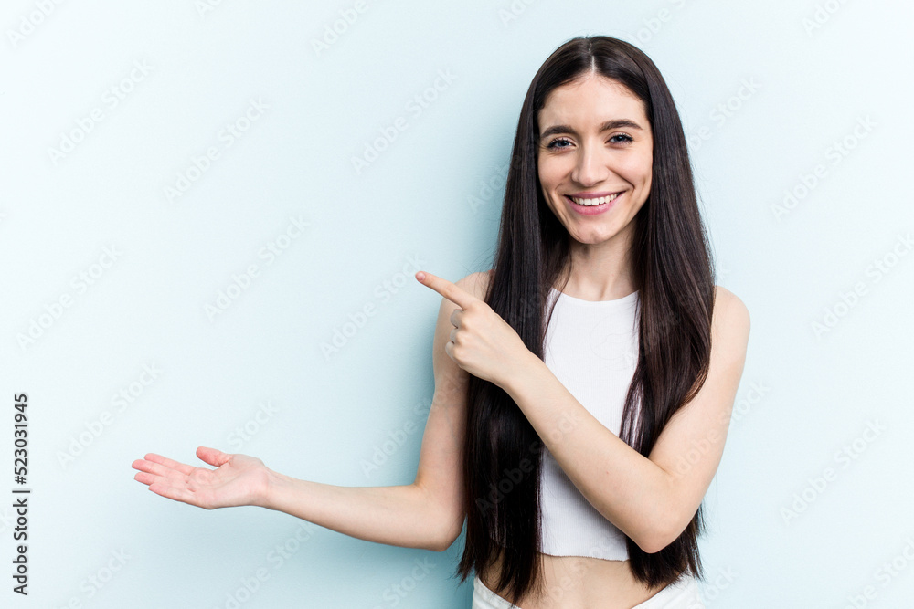 Young caucasian woman isolated on blue background excited holding a copy space on palm. Young caucasian woman isolated on blue background excited holding a copy space on palm.