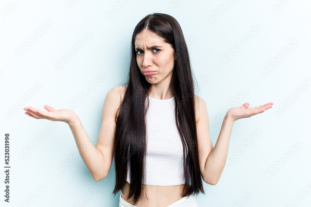 Young caucasian woman isolated on blue background doubting and shrugging shoulders in questioning gesture. Young caucasian woman isolated on blue background doubting and shrugging shoulders in questioning gesture.