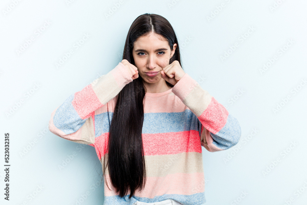 Young caucasian woman isolated on blue background throwing a punch, anger, fighting due to an argument, boxing. Young caucasian woman isolated on blue background throwing a punch, anger, fighting due to an argument, boxing.