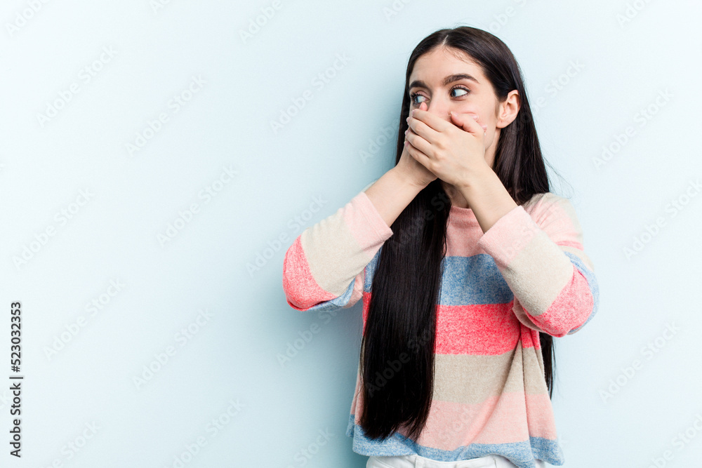 Young caucasian woman isolated on blue background thoughtful looking to a copy space covering mouth with hand. Young caucasian woman isolated on blue background thoughtful looking to a copy space covering mouth with hand.