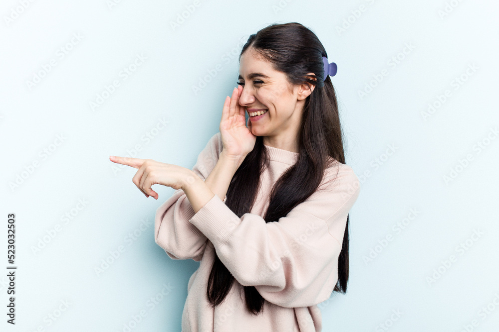 Young caucasian woman isolated on blue background saying a gossip, pointing to side reporting something. Young caucasian woman isolated on blue background saying a gossip, pointing to side reporting something.