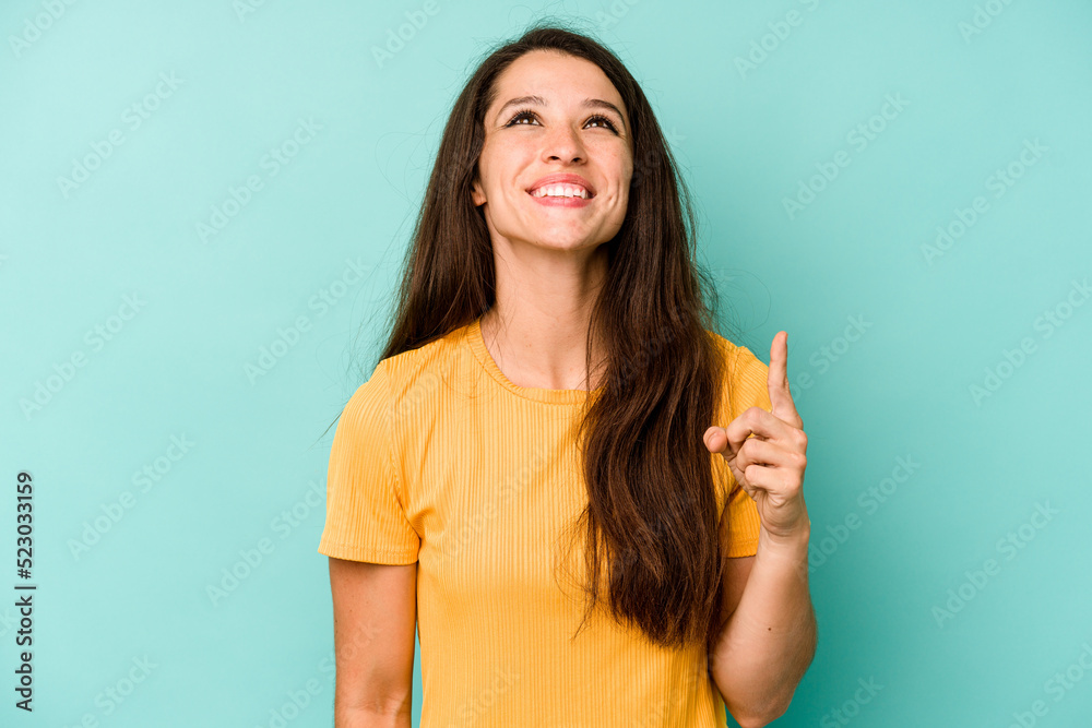 Young caucasian woman isolated on blue background indicates with both fore fingers up showing a blank space. Young caucasian woman isolated on blue background indicates with both fore fingers up showing a blank space.