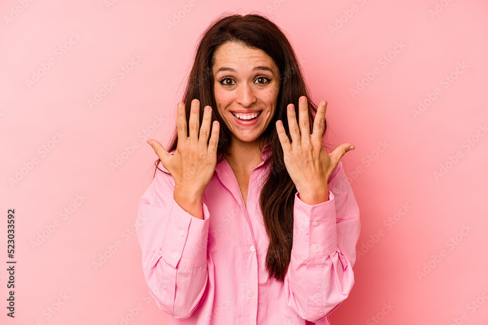 Young caucasian woman isolated on pink background showing number ten with hands.