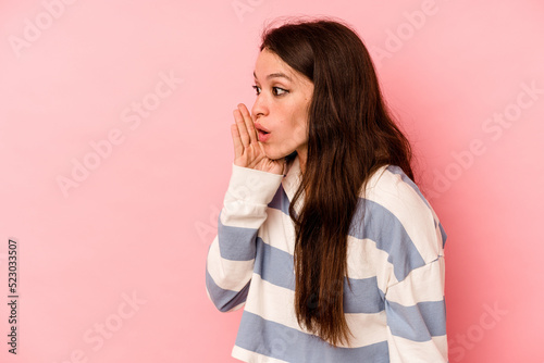 Young caucasian woman isolated on pink background is saying a secret hot braking news and looking aside