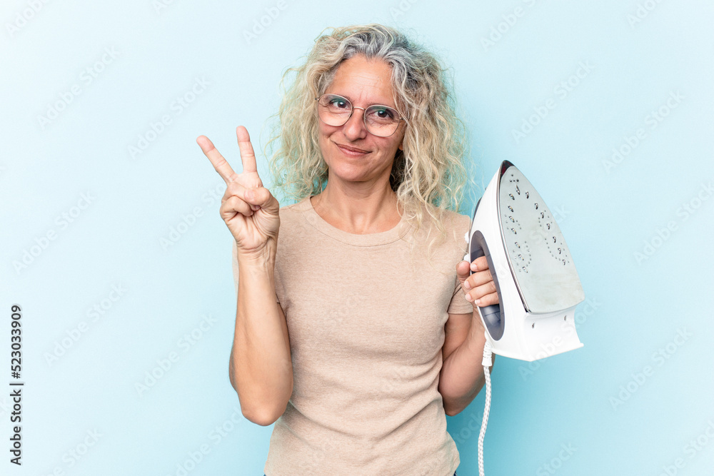 Middle age caucasian woman holding an iron isolated on blue background showing number two with fingers. Middle age caucasian woman holding an iron isolated on blue background showing number two with fingers.
