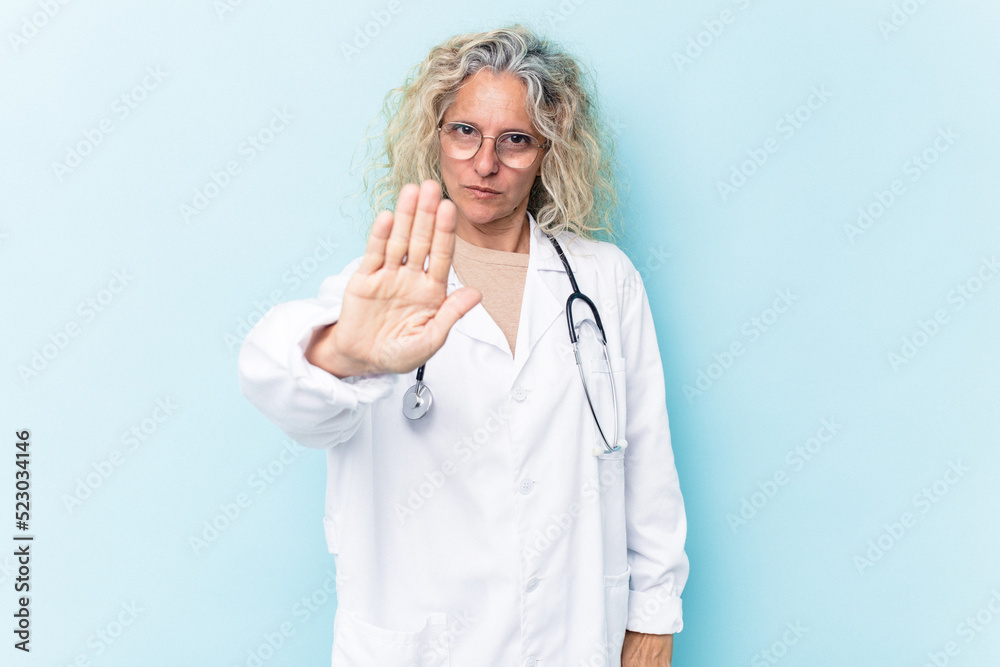 Middle age caucasian woman isolated on blue background standing with outstretched hand showing stop sign, preventing you.