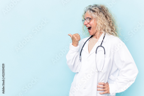 Middle age caucasian woman isolated on blue background points with thumb finger away, laughing and carefree.