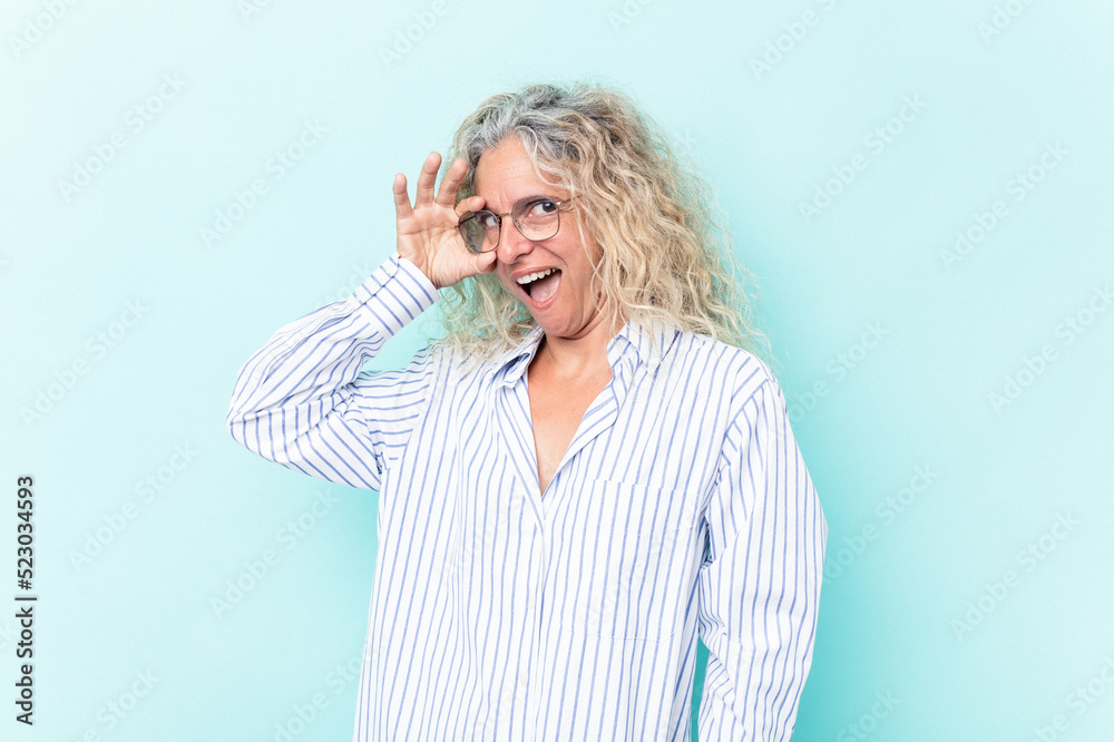 Middle age caucasian woman isolated on blue background excited keeping ok gesture on eye.