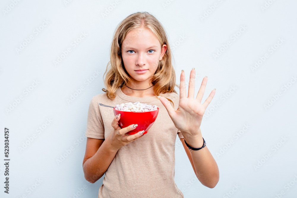 Caucasian teen girl eating cereals isolated on blue background smiling cheerful showing number five with fingers. Caucasian teen girl eating cereals isolated on blue background smiling cheerful showing number five with fingers.