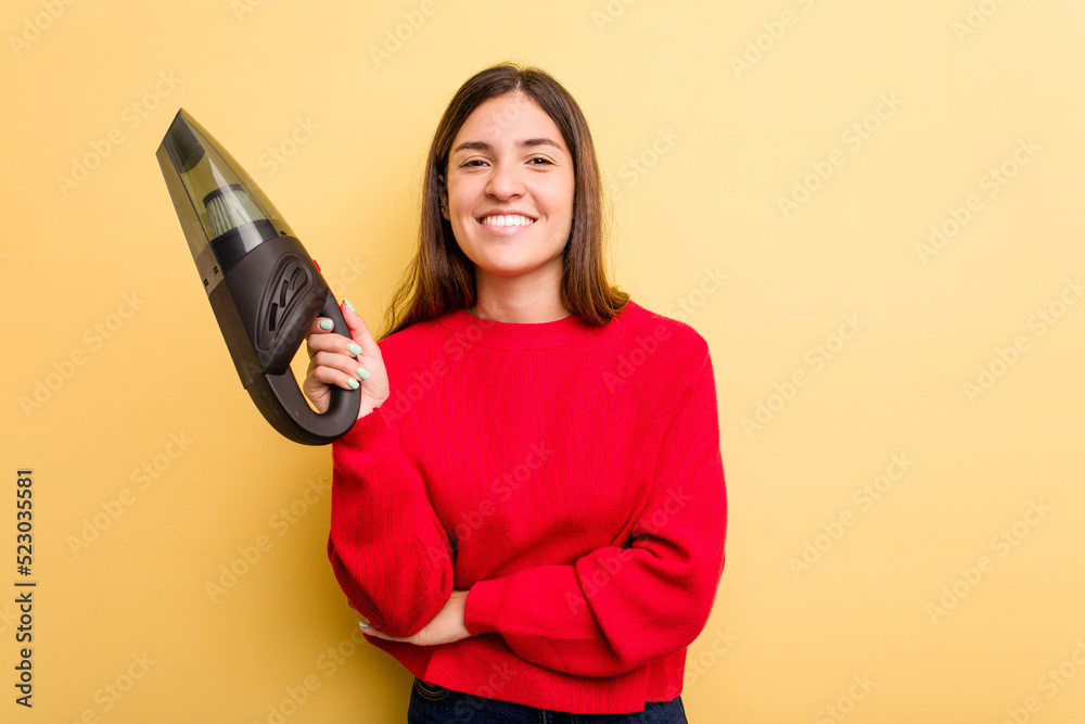 Young caucasian woman holding a hand vacuum cleaner isolated on yellow background laughing and having fun. Young caucasian woman holding a hand vacuum cleaner isolated on yellow background laughing and having fun.