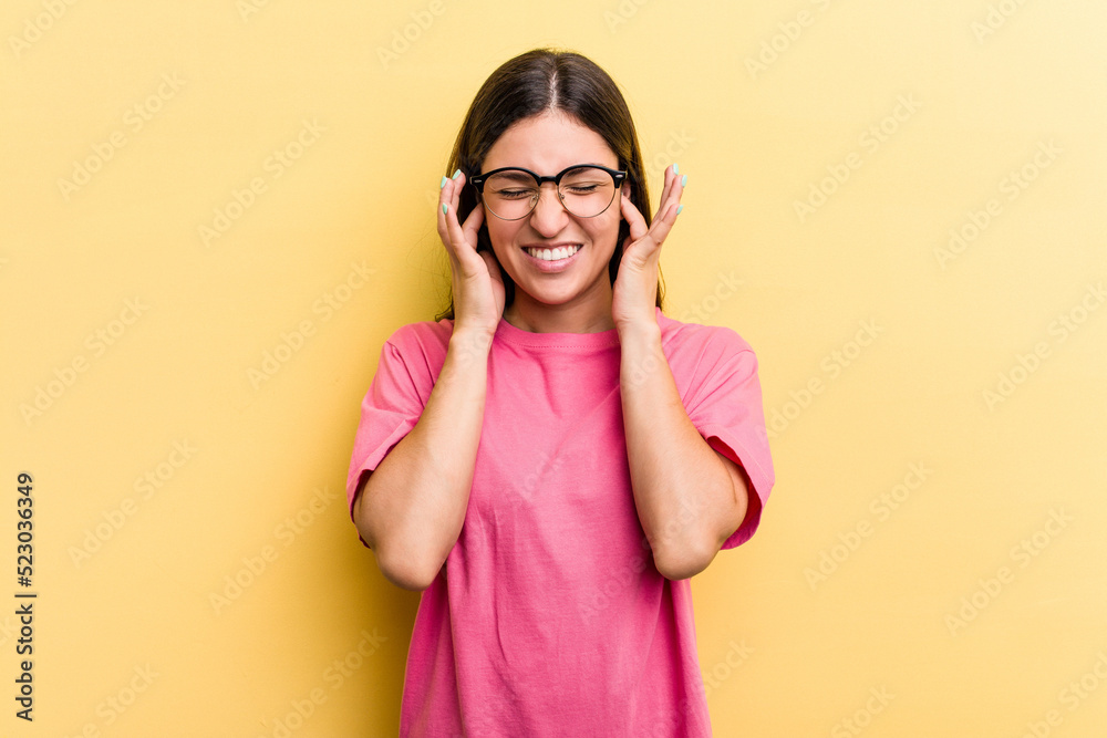 Young caucasian woman isolated on yellow background covering ears with hands.