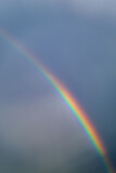Multicolored rainbow on the background of a cloudy sky. Vertical photo