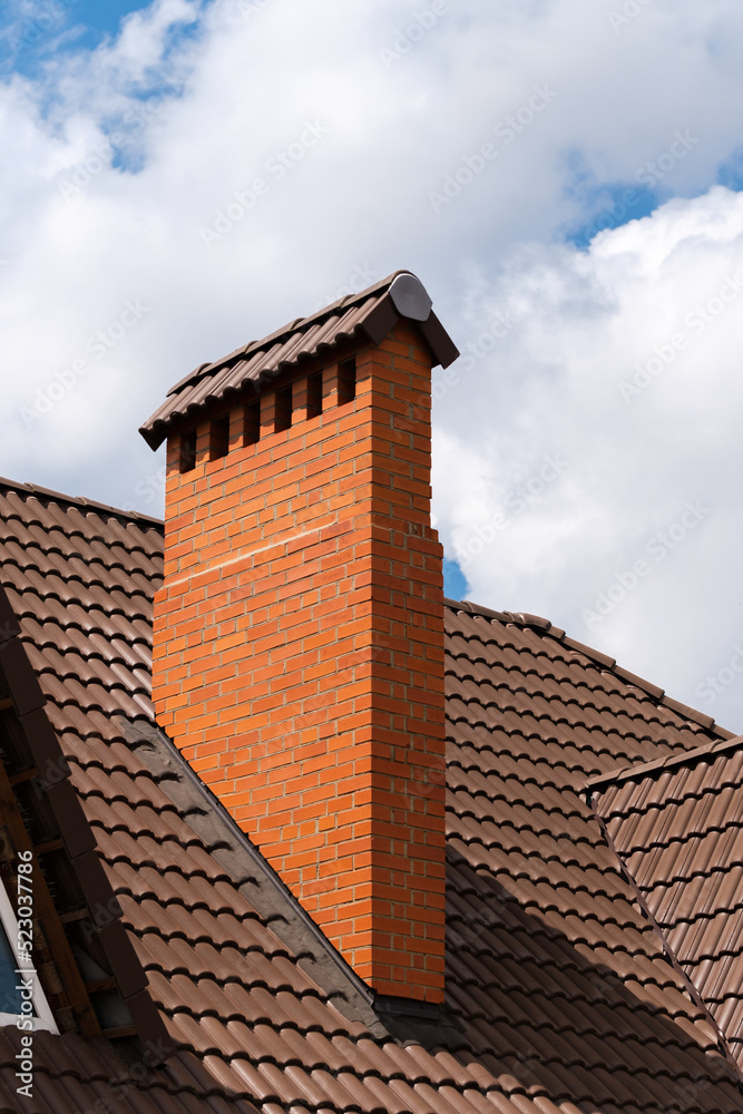 Close up shot of a chimney on a metal tile shingles roof against blue sky with clouds.