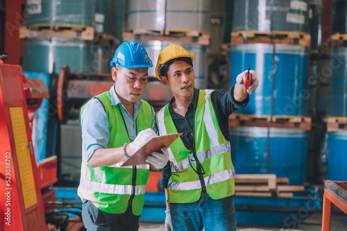 Asian engineer factory manager and mechanic worker employee in safety hard hat talking and inspection inside the factory