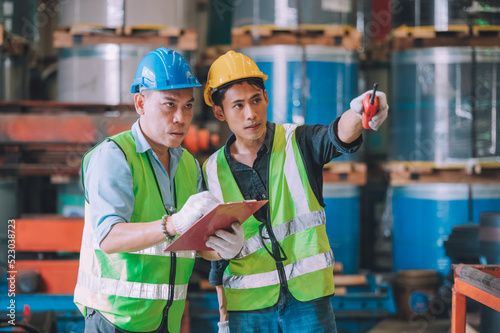 Asian engineer factory manager and mechanic worker employee in safety hard hat talking and inspection inside the factory