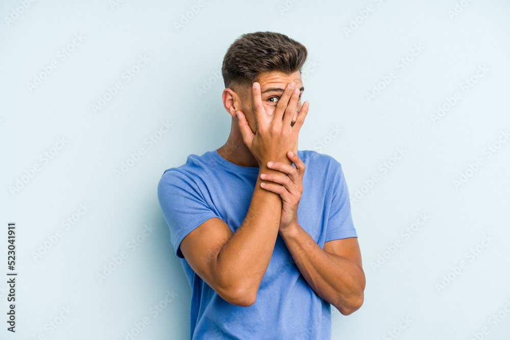 Young caucasian man isolated on blue background blink through fingers frightened and nervous. Young caucasian man isolated on blue background blink through fingers frightened and nervous.
