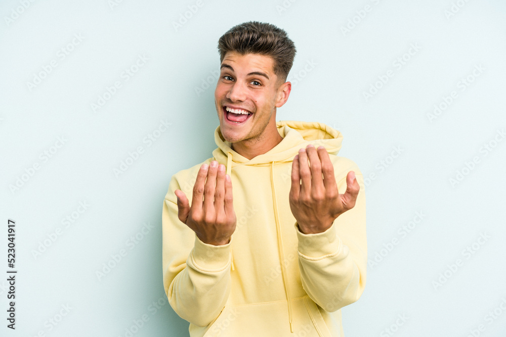 Young caucasian man isolated on blue background pointing with finger at you as if inviting come closer. Young caucasian man isolated on blue background pointing with finger at you as if inviting come closer.