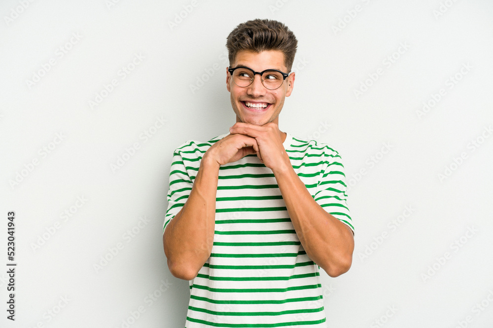 Young caucasian man isolated on white background keeps hands under chin, is looking happily aside. Young caucasian man isolated on white background keeps hands under chin, is looking happily aside.